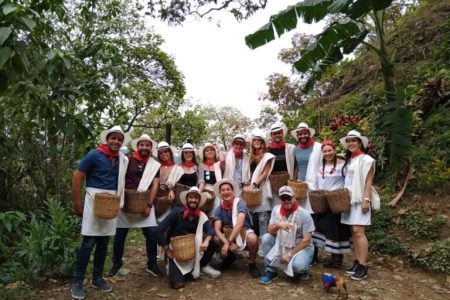 Grupo de viajeros con sombrero, pañoleta roja y canasto de recolección en una finca cafetera cerca de Medellín